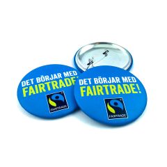 Matta kampanjknappar - perfekta till TV- eller videoframträdanden. Men även mera miljövnänliga då de inte har den tjocka, blanka plastmylaren som blanka knappar har. Här blå knapp med fairtradeloggan på
